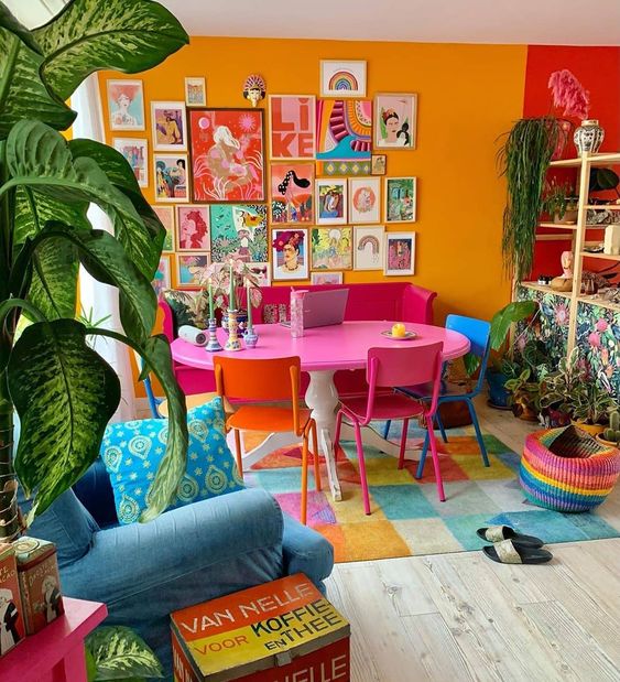 a maximalist dining room with a yellow wall, a pink table, colorful chairs and a rug, a blue chair and a super bold gallery wall