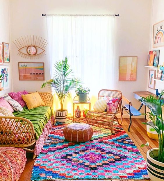 a maximalist living room with a bright boho rug, rattan furniture, colorful pillows, artwork and books is a lovvely and fun space