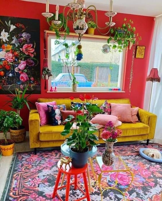a maximalist living room with a red accent wall, a yellow sofa, a colorful rug and some bold art, pillows and greenery