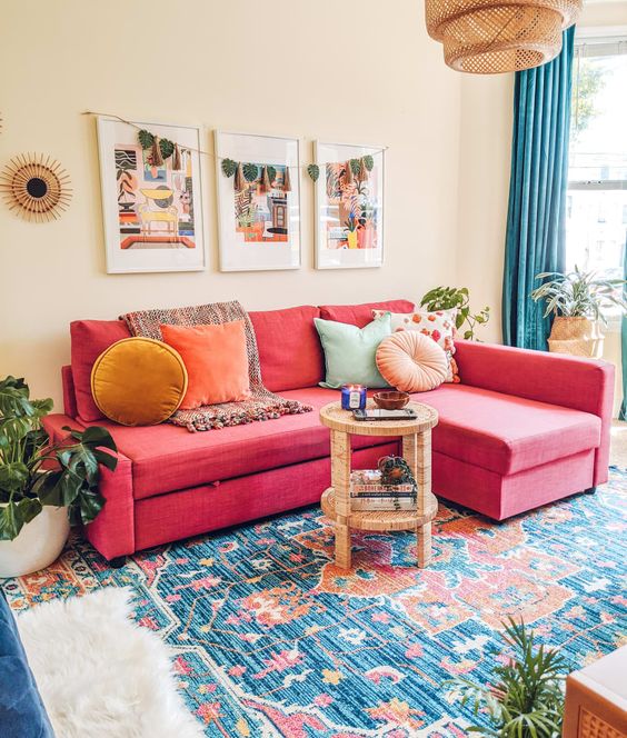 a maximalist living room with a red sofa and colorful pillows, a colorful rug, a gallery wall and a woven pendant lamp