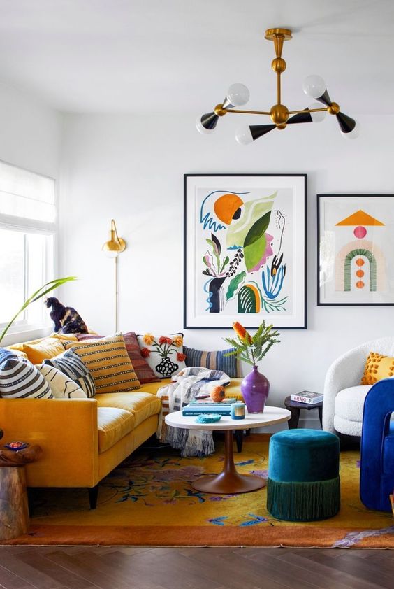 a maximalist living room with a yellow sofa and colorful pillows and a rug, a blue pouf and bold blue chair, some bright artwork