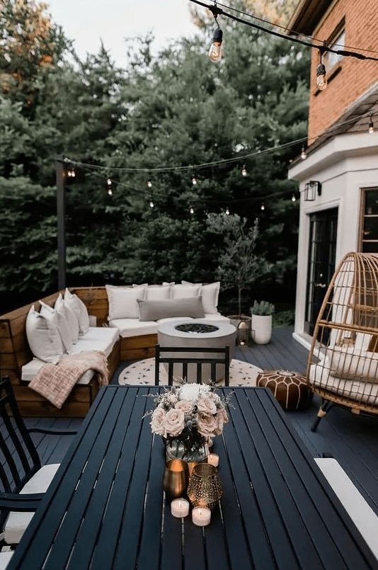 A modern and bold farmhouse terrace with a black deck, a built in bench with upholstery, a rattan egg chair, a black planked dining set