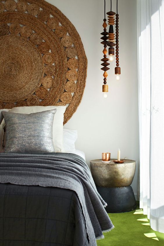 a modern boho bedroom with a bed and grey bedding, a jute rug on the wall, pendant lamps with wooden beads and a metal side table