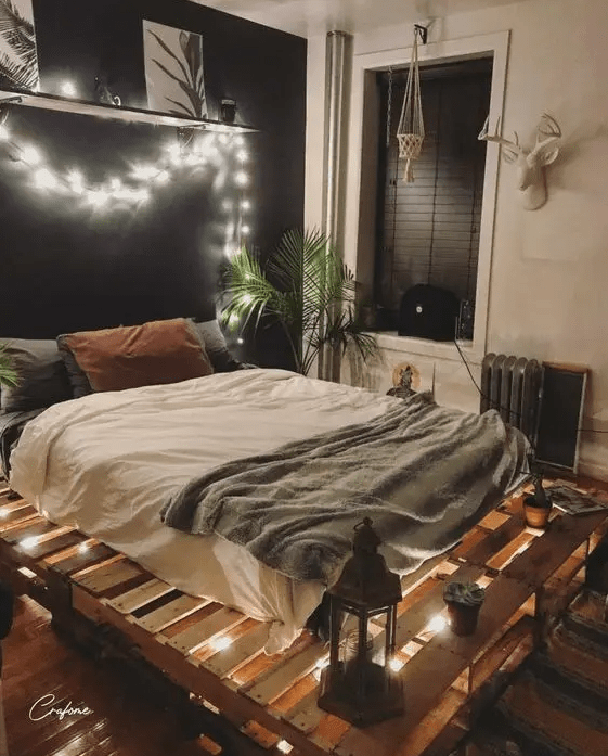 a modern boho bedroom with a black accent wall, a pallet bed with lights inside, lanterns and a statement plant