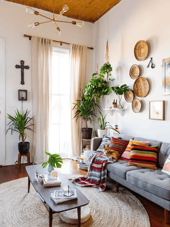 a modern boho living room with a grey sofa, a coffee table, boho pillows, a gallery wall, potted greenery and a chandelier