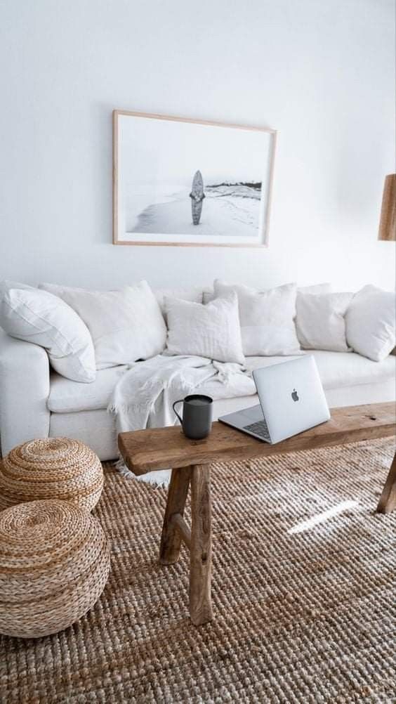 a modern coastal living room with a jute rug, a white sofa, jute poufs, a bench and some coastal decor