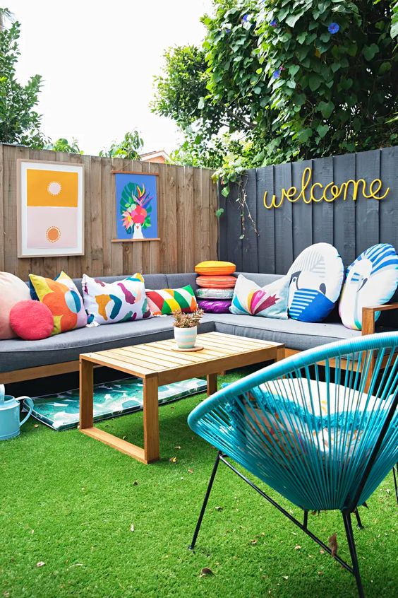 a modern colorful terrace with a green lawn, a grey sectional with colorful pillows, a blue chair, some colorful decor