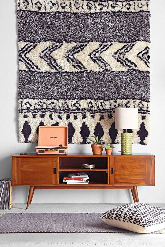 a modern credenza with some stuff and decor, a black and white boho rug on the wall and a neutral rug on the floor