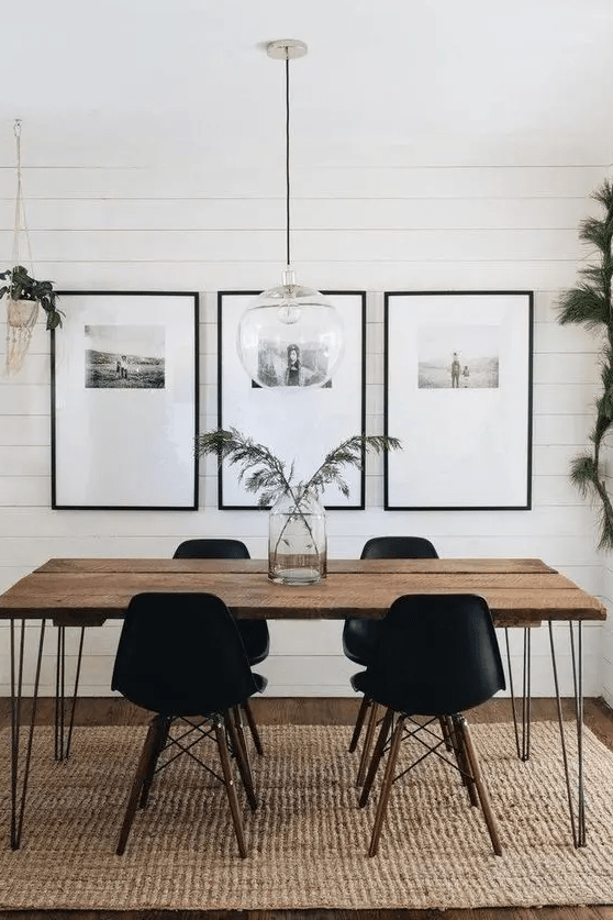 a modern dining room with a hairpin leg table, black chairs, a gallery wall and some greenery
