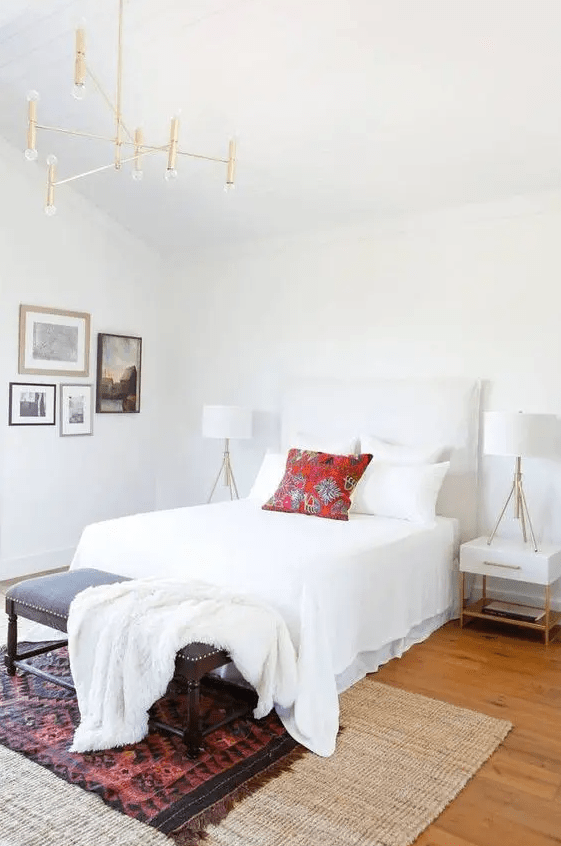 a modern farmhouse bedroom with layered rugs, a bed with white bedding, nightstands and lamps and a gallery wall