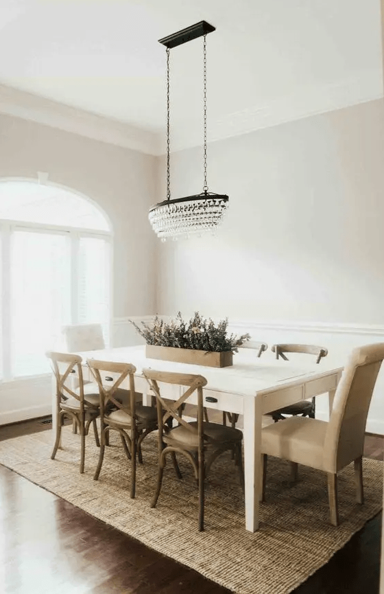 a modern farmhouse dining room with a white table, stained chairs, a crystal pendant lamp and a jute rug for a textured touch