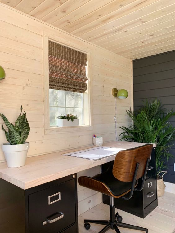 a modern farmhouse home office with planked walls, floro and ceiling, a black accent wall, a black desk and a comfy chair