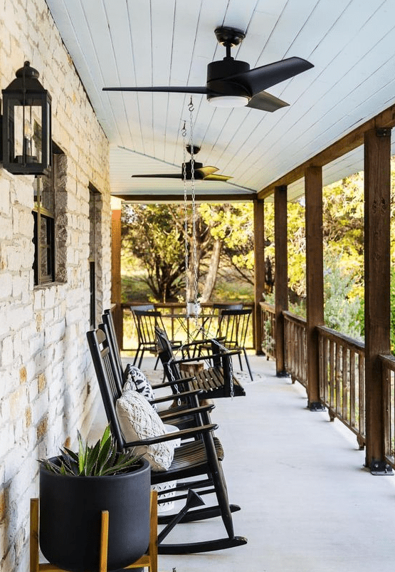 a modern farmhouse porch with black rockers and a bench on chains, modern black planters and chic lanterns on the walls