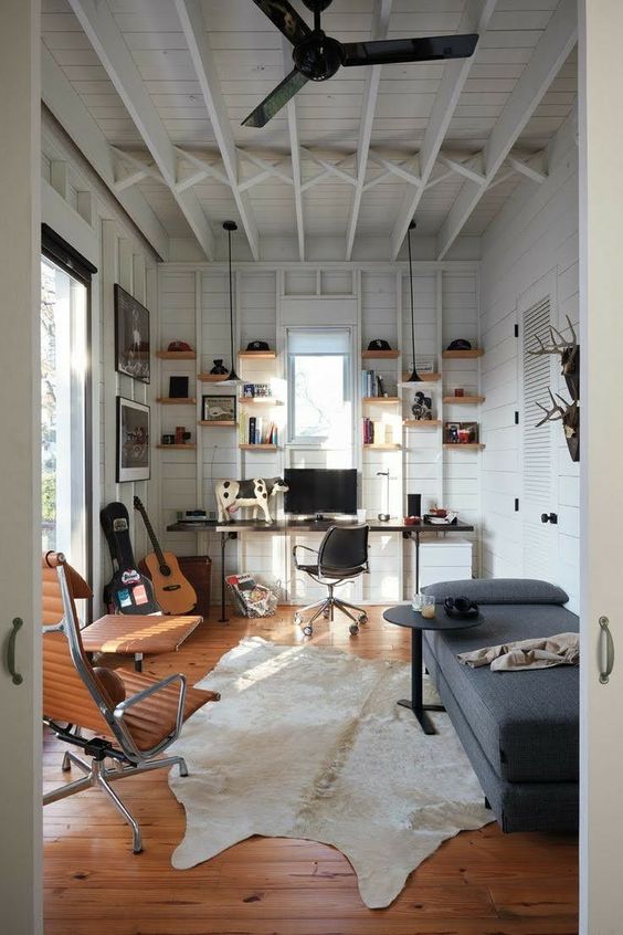 a modern farmhouse shed home office with a desk, shelves, a grey daybed, a side table, amber leather chairs and lamps