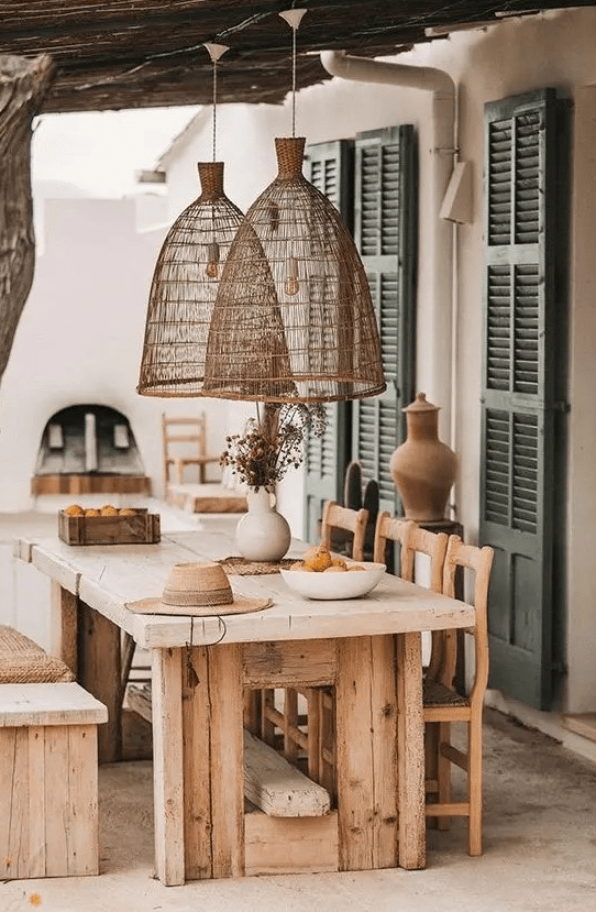 a modern farmhouse terrace with a roof and woven lamps, with a rough wood dining set and a hearth is a lovely space to have a meal