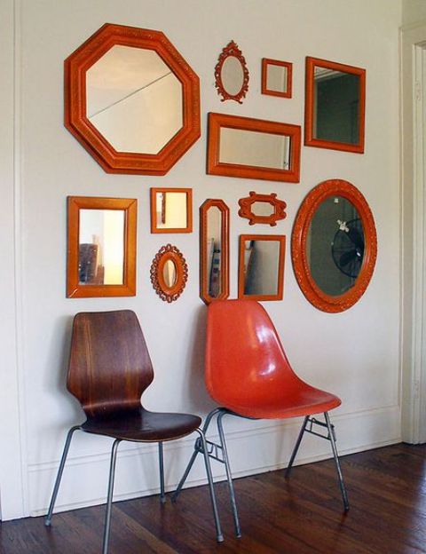 a modern gallery wall of mirrors in red frames to add a bit of color to the space, with stained and red chairs