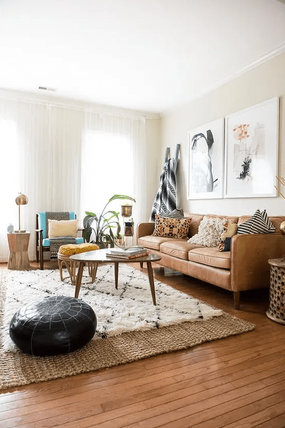 a modern living room with a tan leather couch, some chairs, a coffee table, layered rugs including a jute one, some chic decor