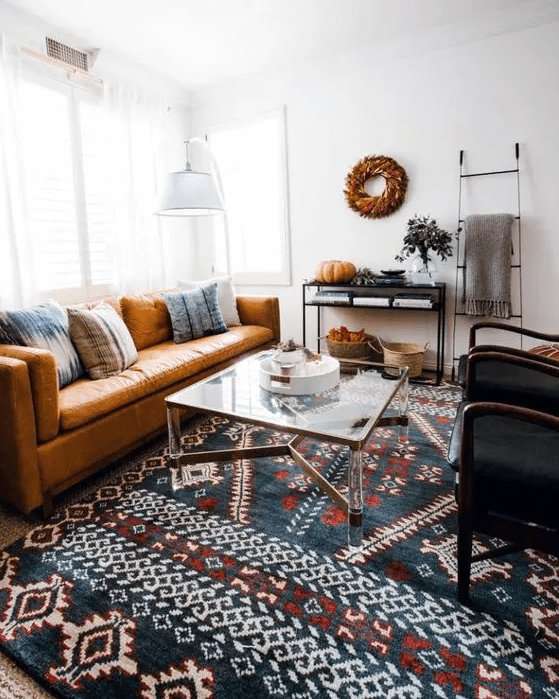 a modern living room with an amber leather couch with pillows, a bold printed rug, a coffee table, a console table and black chairs
