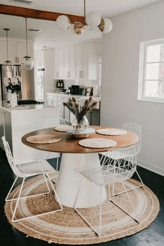 a modern neutral dining space with a jute rug, a round table, white metal chairs, a modern chandelier is a lovely and cozy nook