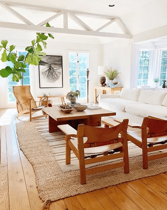 a modern neutral living rom with a white sofa, a coffee table, leather chairs, layered rugs including a jute one, greenery and chic decor on the table in the corner