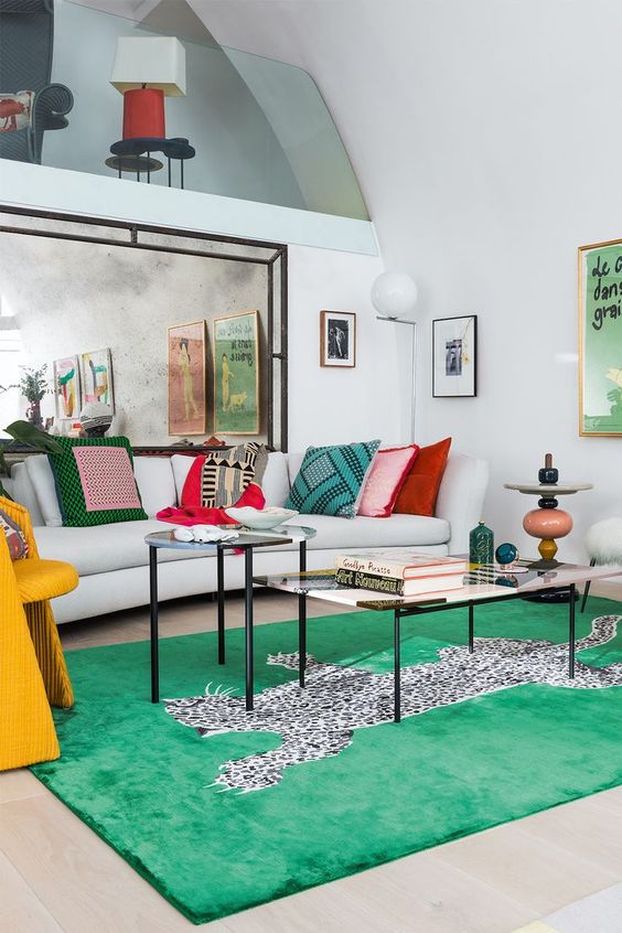 a modern neutral living room with a neutral sofa and colorful pillows, a bold green rug, a yellow chair and some bright decor
