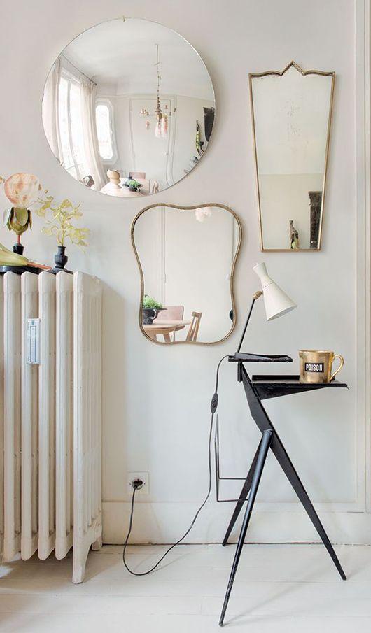 a modern nook accented with mismatching chic mirrors, a tiny stand with a lamp and a mug and a radiator with decor