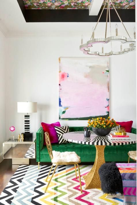 a modern refined living room with a floral ceiling, a green sofa with colorful pillows, a bold chevron rug, a striped table and some bright details
