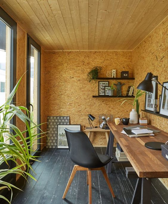a modern shed home office with a large trestle desk, a black chair, black ledges with decor and plants is amazing