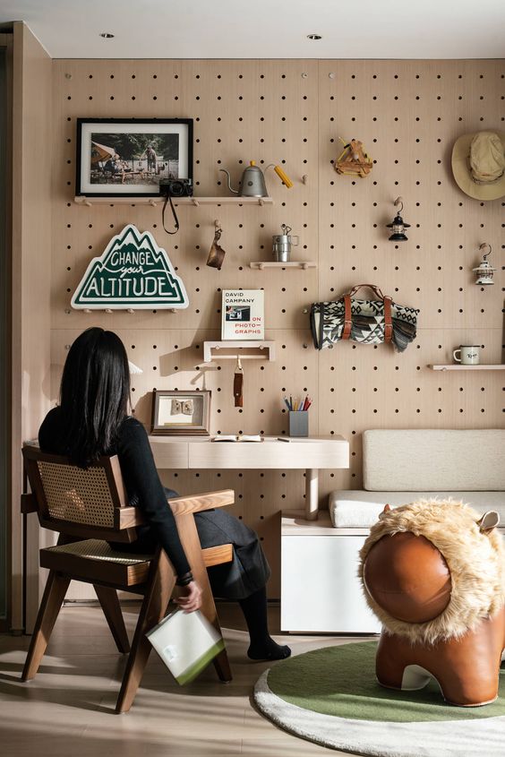 a modern space with a pegboard wall, with shelves and hooks, a built-in desk and an upholstered bench plus a cane chair is wow