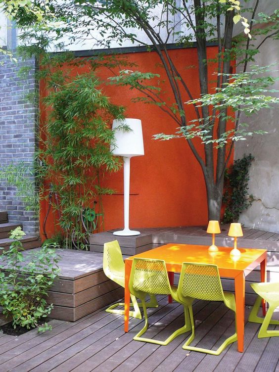 a modern terrace with a deck, an orange table, yellow chairs, yellow lamps and greenery and trees