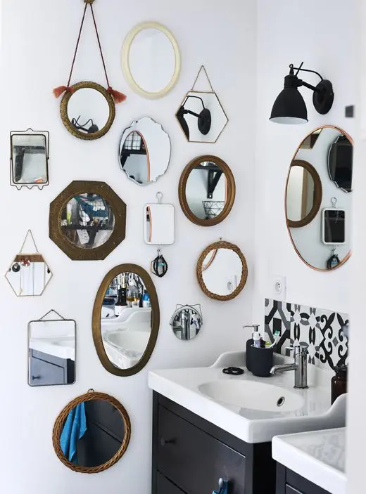 a monochromatic bathroom with a gallery wall of mismatching mirrors and black wall lamps, black vanities and black and white tiles