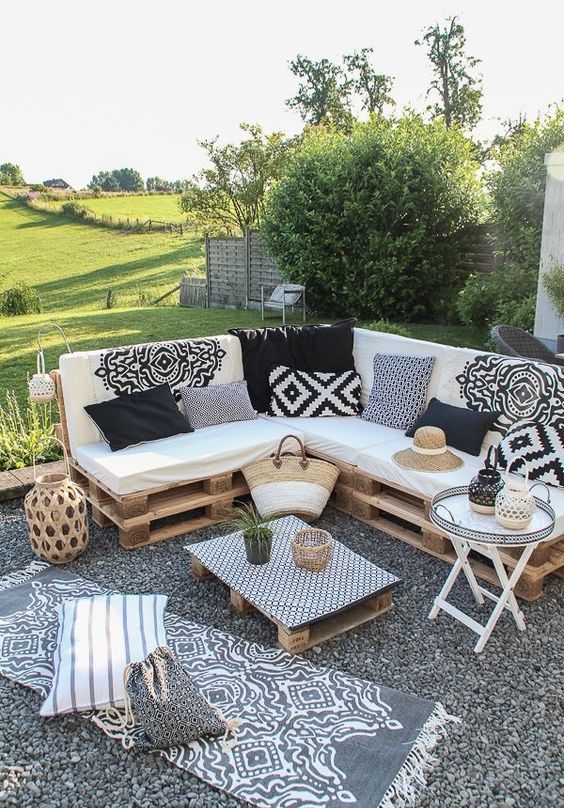 a monochromatic boho terrace with a pallet corner sofa and boho pillows, a small table, a pallet coffee table and some rugs and pillows
