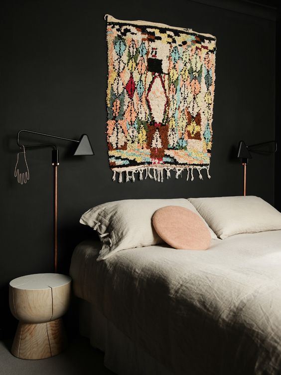 a moody black bedroom with a bed and neutral bedding, a bright boho rug to add color, insterest and print to the space