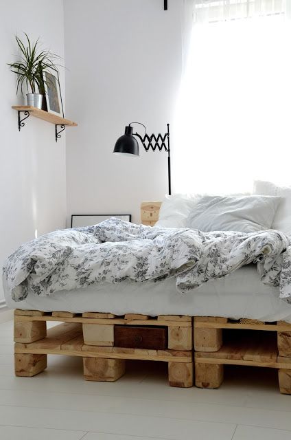 a neutral Scandinavian bedroom with a pallet bed and neutral bedding, a shelf with decor and a black wall lamp