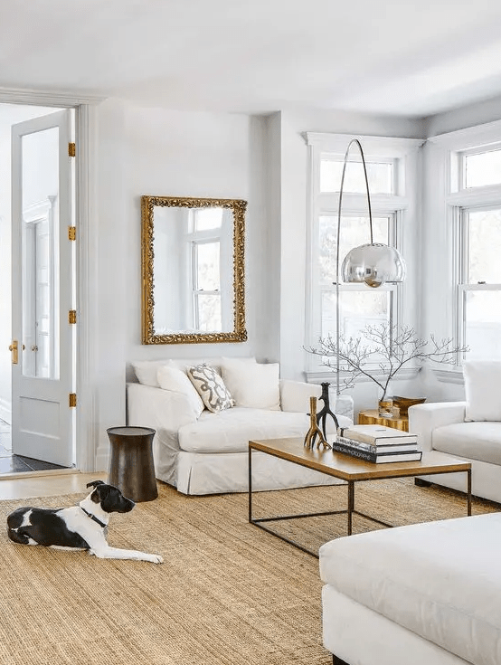 a neutral and airy living room with neutral seating furniture, a coffee table, a jute rug, a floor lamp and a mirror in a chic frame
