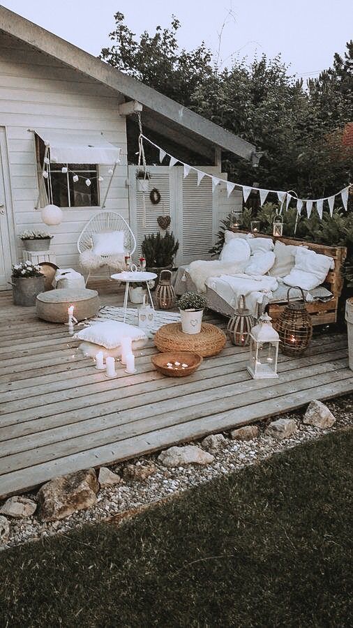a neutral boho terrace with a pallet sofa and pillows, poufs and cushions, a chair, candle lanterns and lights