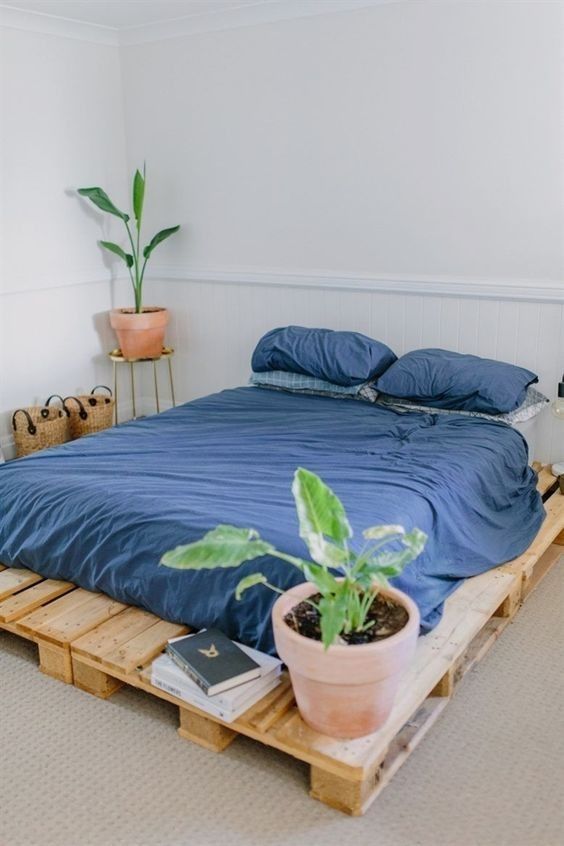 a neutral guest bedroom with a pallet bed and navy bedding, baskets for storage and some potted plants is cool
