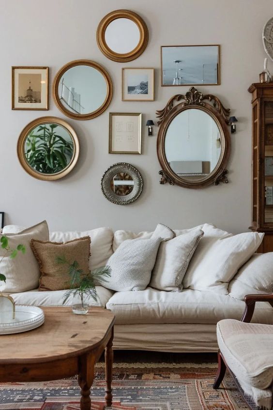a neutral living room with a mirror gallery wall, a white sofa with pillows, a white chair, a stained table and a boho rug