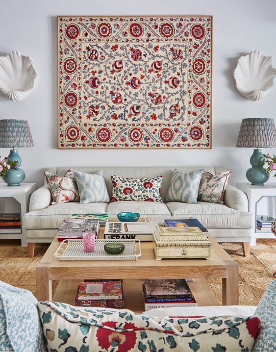 a neutral living room with neutral sofas and colorful pillows that echo with the rug on the wall, some whimsical decor and books