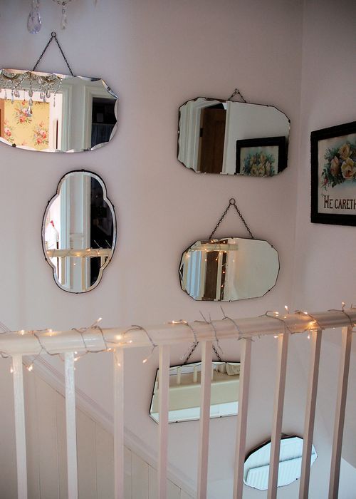 a neutral wall over the stairs done with mismatching mirrors and soem art plus lights on the railing looks very chic