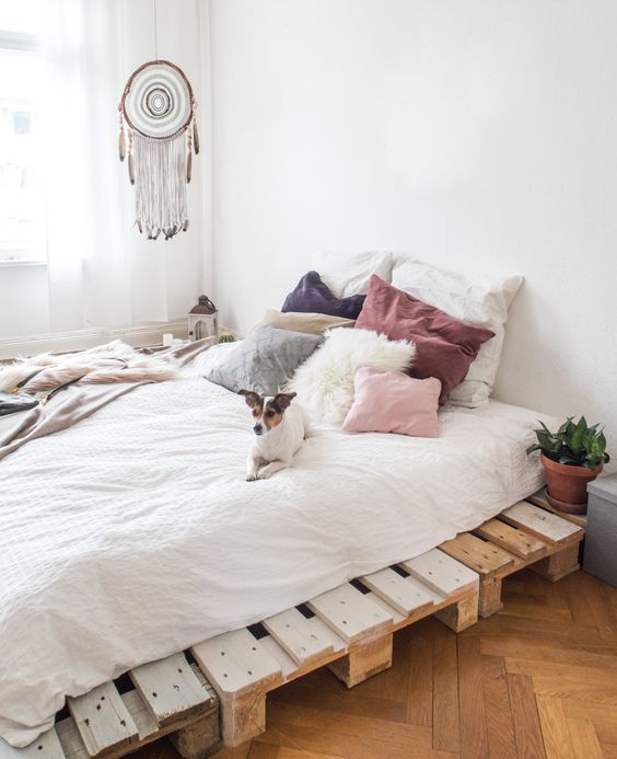 a pallet bed with neutral bedding, potted plants and a dream catcher and blankets for a serene boho bedroom