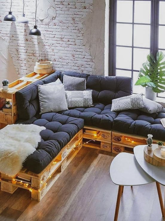 a pallet sofa with black cushions and boho pillows, a duo of tables and pendant lamps plus lights inside the sofa