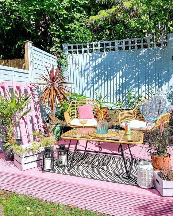 a pink terrace with rattan furniture, a pink pallet, lanterns, potted plants and some bright tableware