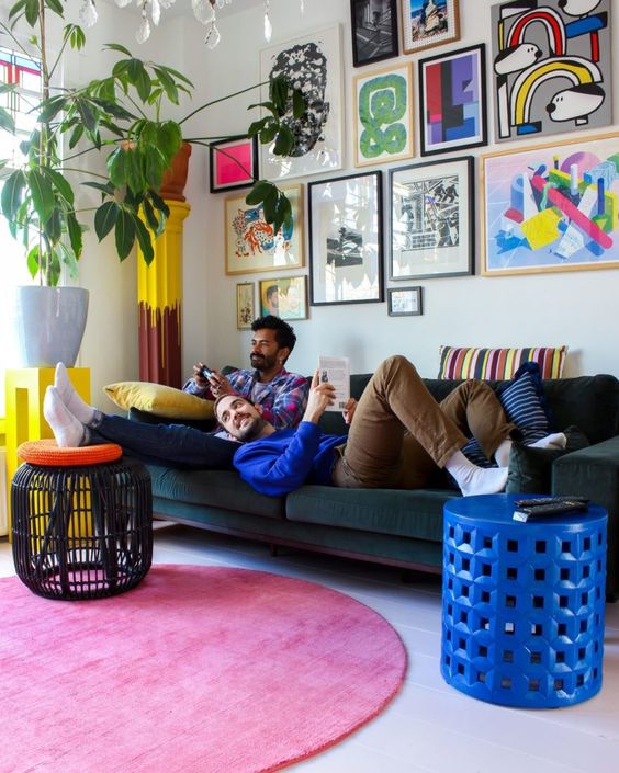 a playful living room with a dark green sofa, a pink rug, some side tables, a bold gallery wlal and a large plant