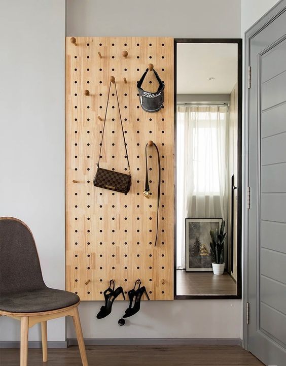 a pretty and modern entryway solution with a pegboard with hooks and a mirror attached to the wall are great to organize a space