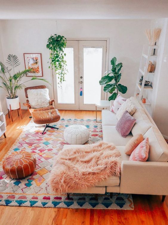 a pretty boho living room with a neutral sectional and pastel pillows, a bright rug, an amber leather chair and some greenery