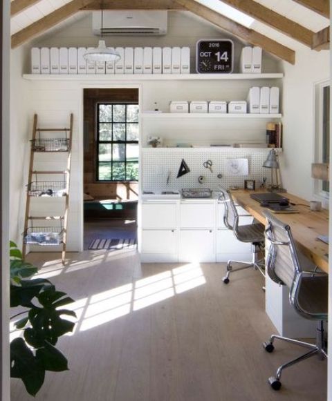 a pretty modern shed home office with shelves with various necessary stuff, a chest of drawers, a double desk with chairs, and a pendant lamp