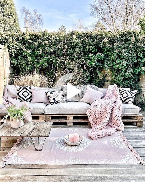 a pretty pink boho terrace with a pallet sofa and boho pillows, a reclaimed wood table, pink textiles and a living wall