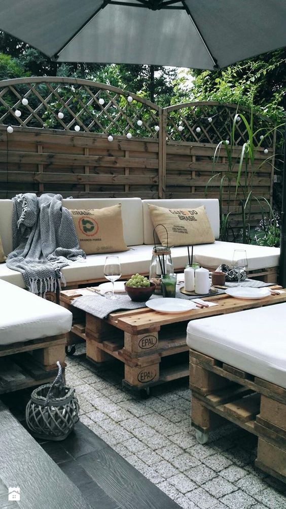 a pretty terrace with pallet furniture, some pillows and blankets, lights and greenery is a lovely space