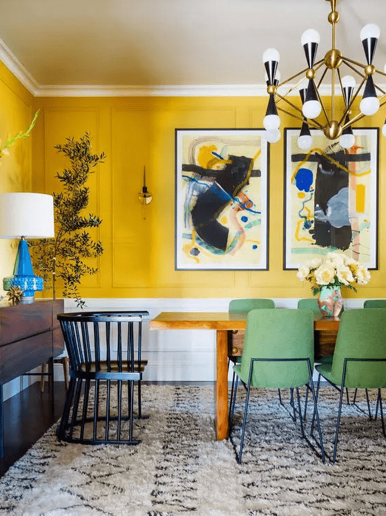 a quirky dining room with yellow walls, a bold gallery wall, a wooden table and green chairs, a retro chandelier and a potted plant